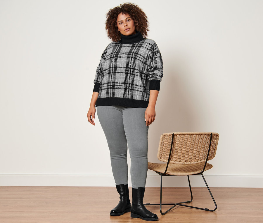 Frau posiert in Strickpullover mit Rollkragen, hellgrauen Treggings und Lederboots.