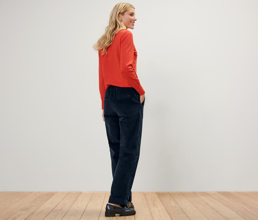 Frau posiert in Cord-Joggpants und orangefarbenem Pullover.