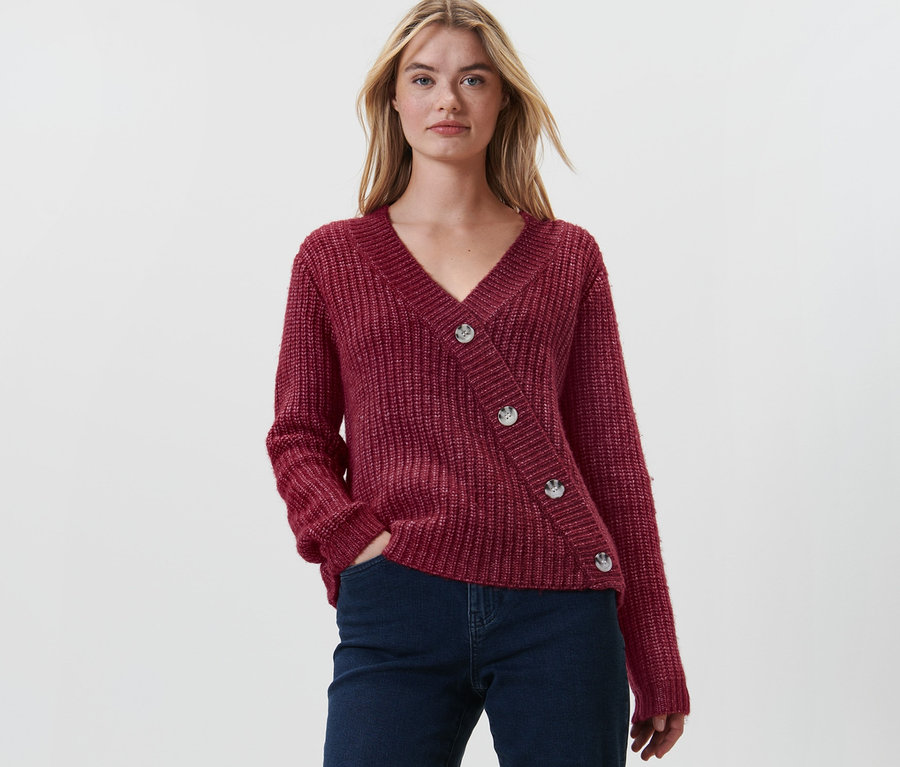 Frau posiert in rotem Grobstrick-Cardigan und dunkler Jeans.