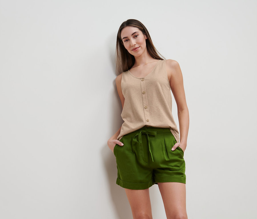 Frau posiert in beige meliertem Top mit Knopfleiste und grünen Shorts.
