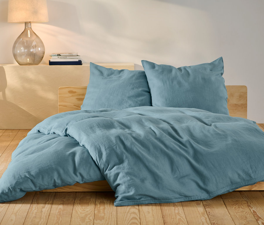 Blaue Leinen-Bettwäsche in Normalgröße und Übergröße auf einem Bett.