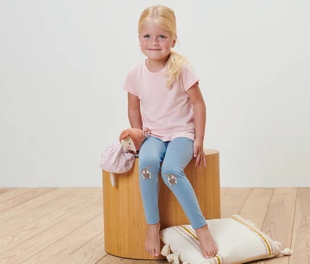 Ein Mädchen sitzt auf einem Hocker und trägt 2 Baby-Leggings mit Streifen.