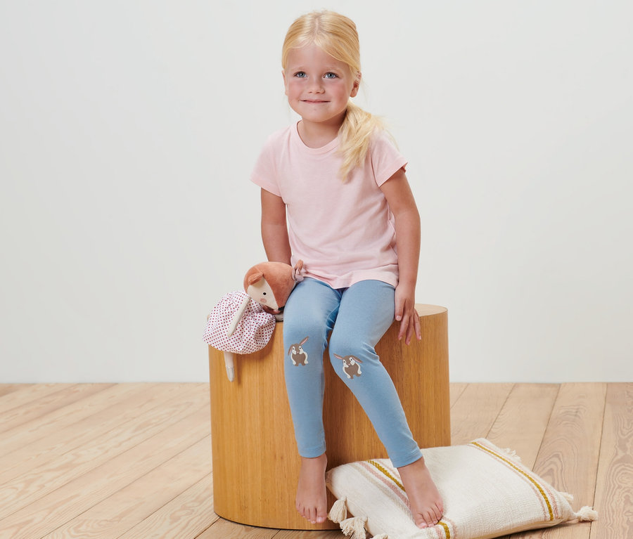 Ein Mädchen sitzt auf einem Hocker und trägt 2 Baby-Leggings mit Streifen.