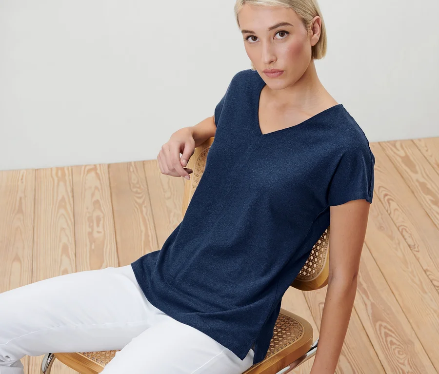 Blonde Frau sitzt auf einem Stuhl und trägt ein dunkelblaues Shirt mit Leinen.