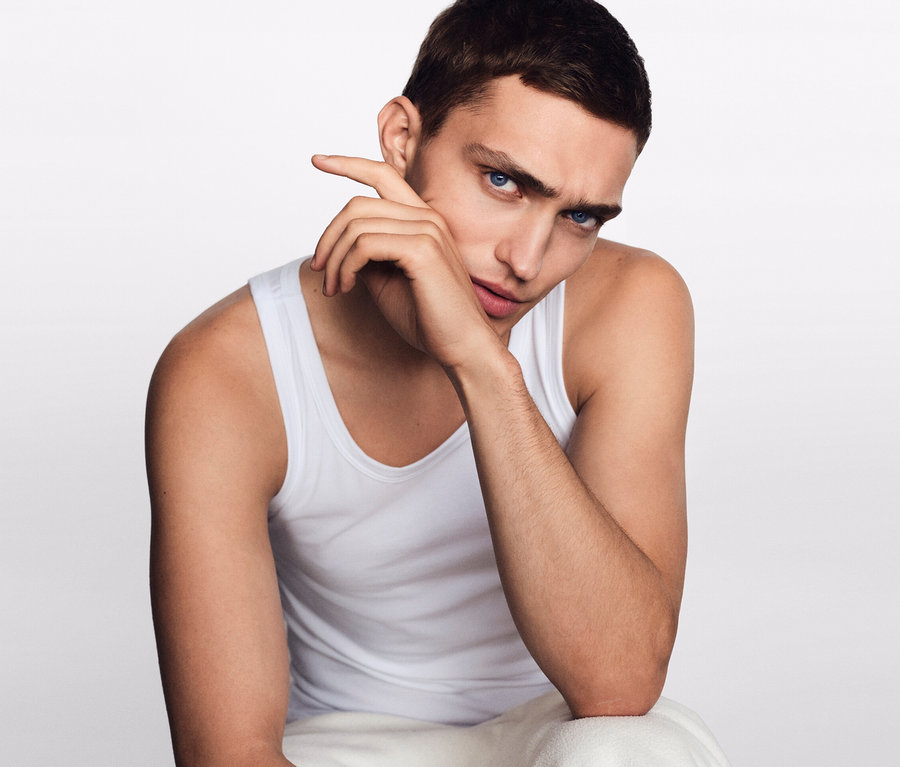 Mann sitzt mit der Hand am Gesicht. Er trägt 2 SCHIESSER Unterhemden mit Bio-Baumwolle, weiß.