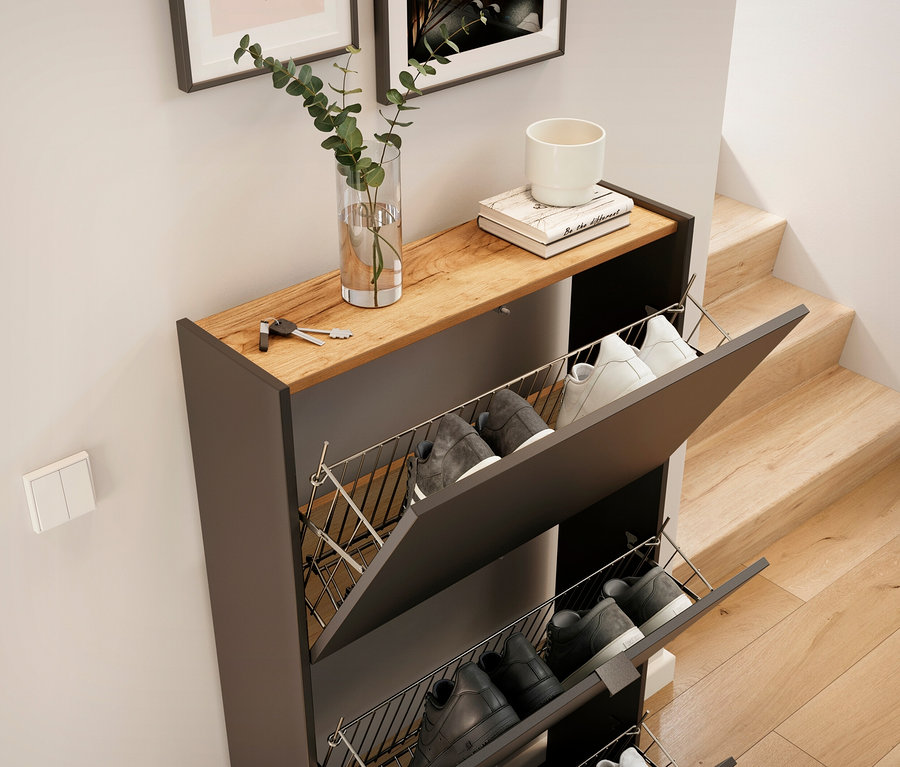 Schwarzer Schuhschrank mit drei offenen Fächern mit Schuhen, oben drauf Vase mit Pflanze, Buch und weisse Tasse.