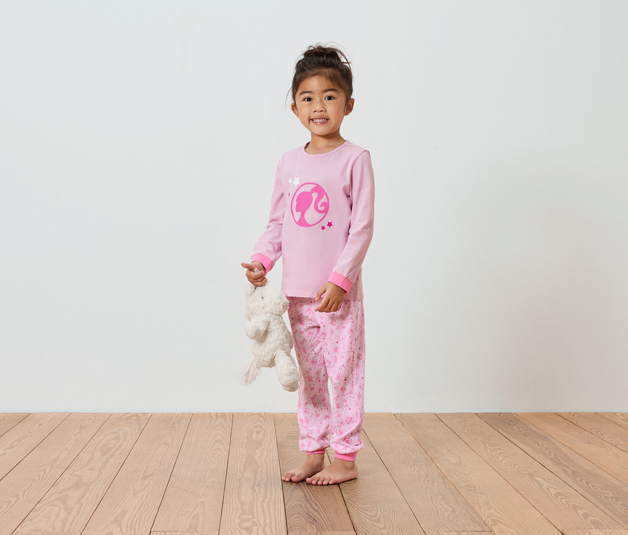 Mädchen im rosa Barbie-Pyjama hält einen Teddybären.