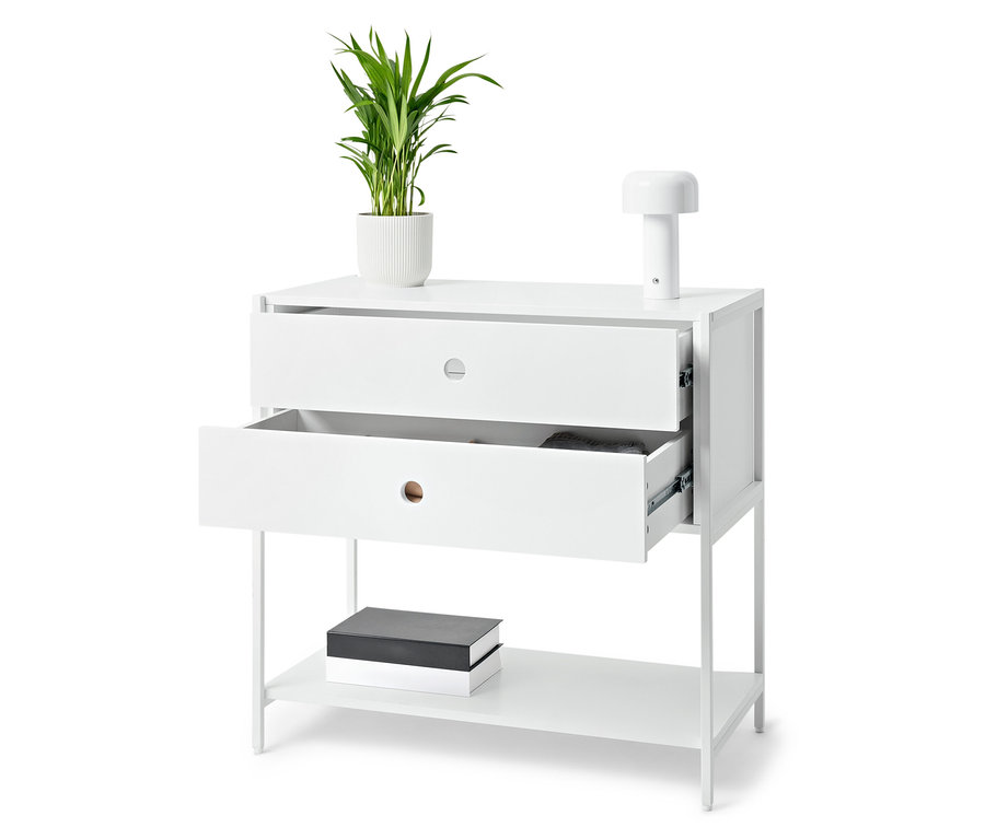 Weißer Tisch mit zwei Schubladen, von denen eine geöffnet ist, auf dem eine Topfpflanze und eine Lampe stehen. Auf dem unteren Regal liegen Bücher.