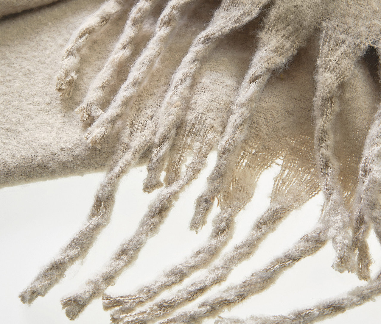 Detailaufnahme eines beigen Schals mit Fransen.