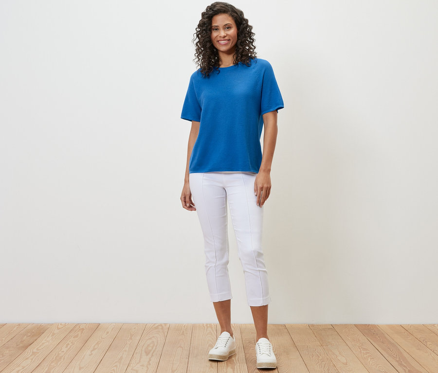 Frau trägt ein kobaltblaues Feinstrick-Shirt, weiße Hosen und weiße Turnschuhe.