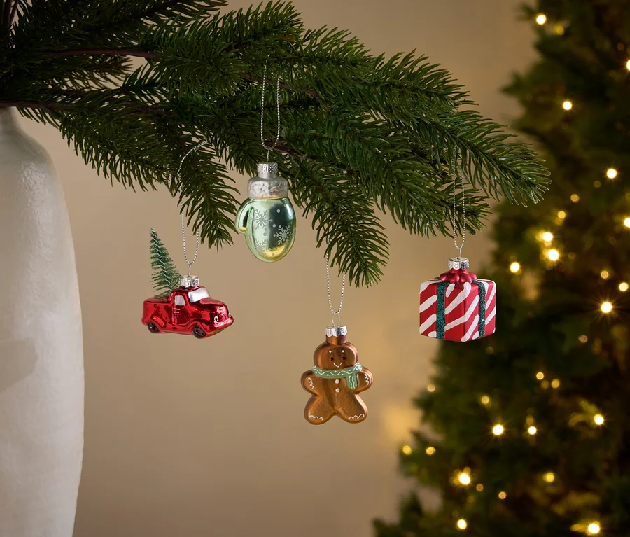 Zweige eines Weihnachtsbaums mit Ornamenten in Form eines roten Autos mit Weihnachtsbaum, eines Handschuhs, eines Lebkuchenmanns und eines Geschenks.