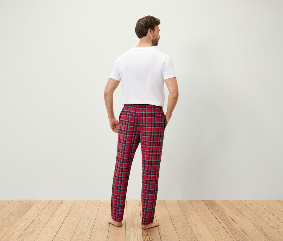 Mann mit dem Rücken zur Kamera hat die Hände in den Taschen einer rot karierten Pyjamahose und ein weißes T-Shirt.