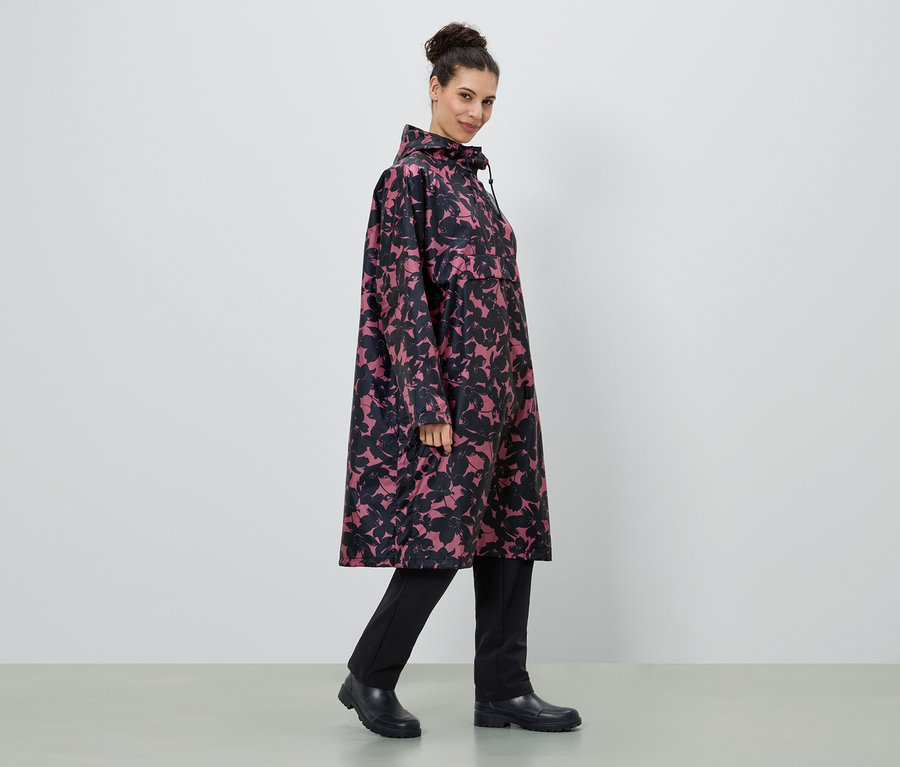 Frau trägt einen langen Regenmantel mit Blumenmuster in Pink und Schwarz, dazu schwarze Hose und Stiefel.