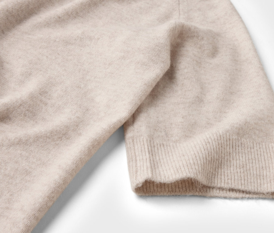 Nahaufnahme eines beigen Strickpullovers mit kurzem Ärmel auf weißem Hintergrund.