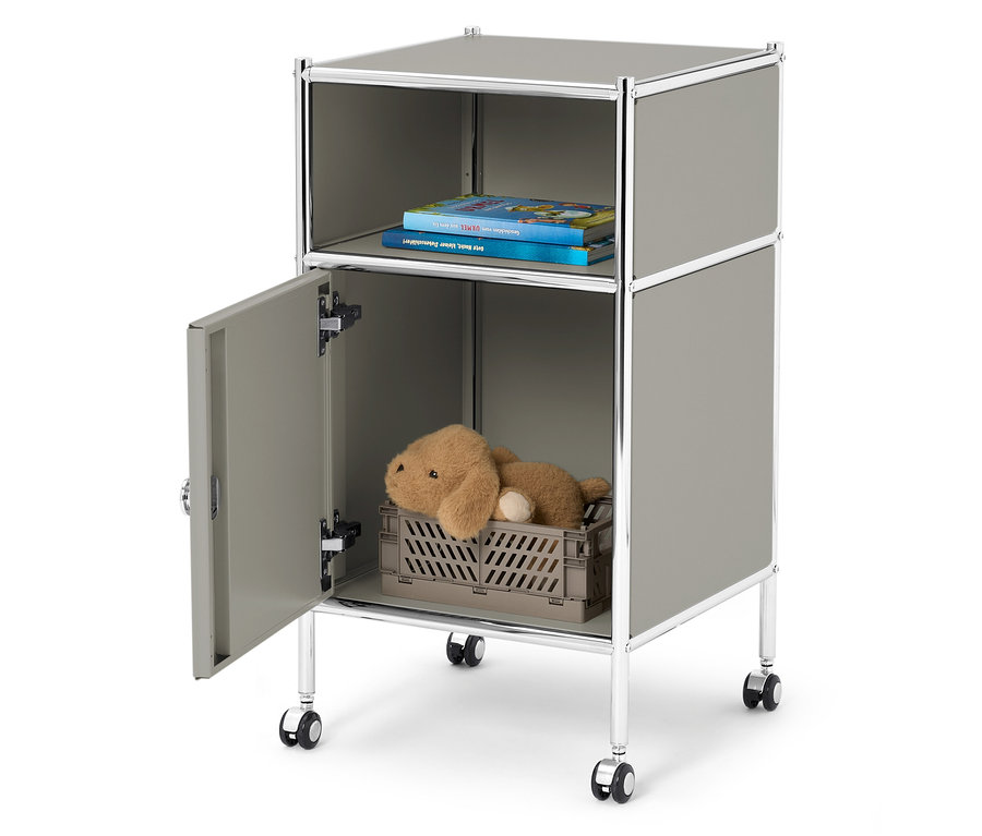 Ein grauer Rollcontainer mit offenem Fach oben mit zwei Büchern und einem offenen Fach unten mit einem Teddybären in einer grauen Kiste.