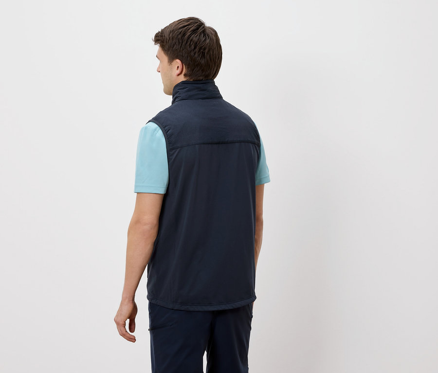 Ein Mann steht mit dem Rücken zur Kamera und trägt eine marineblaue Weste über einem hellblauen T-Shirt.