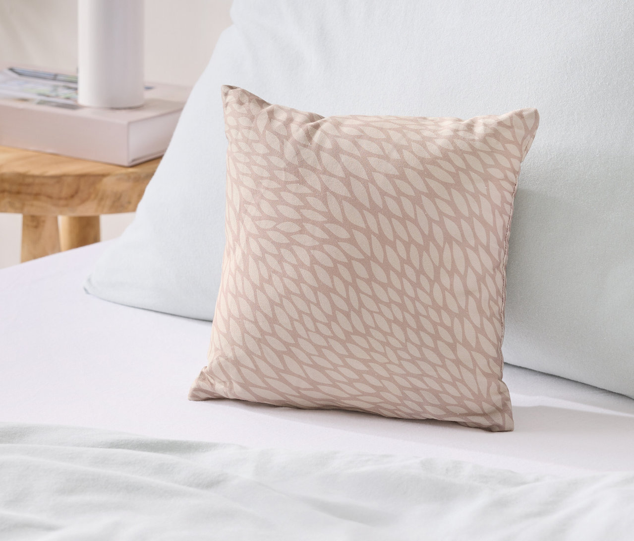 Ein beiges Kissen mit Blattmuster liegt auf einem Bett neben einem blauen Kissen.