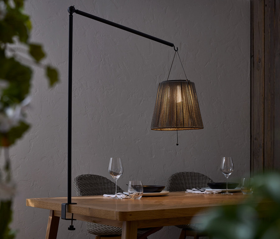 Esstisch mit Geschirr und Lampe mit schwarzem Lampenschirm, die an einer schwarzen Stange befestigt ist.