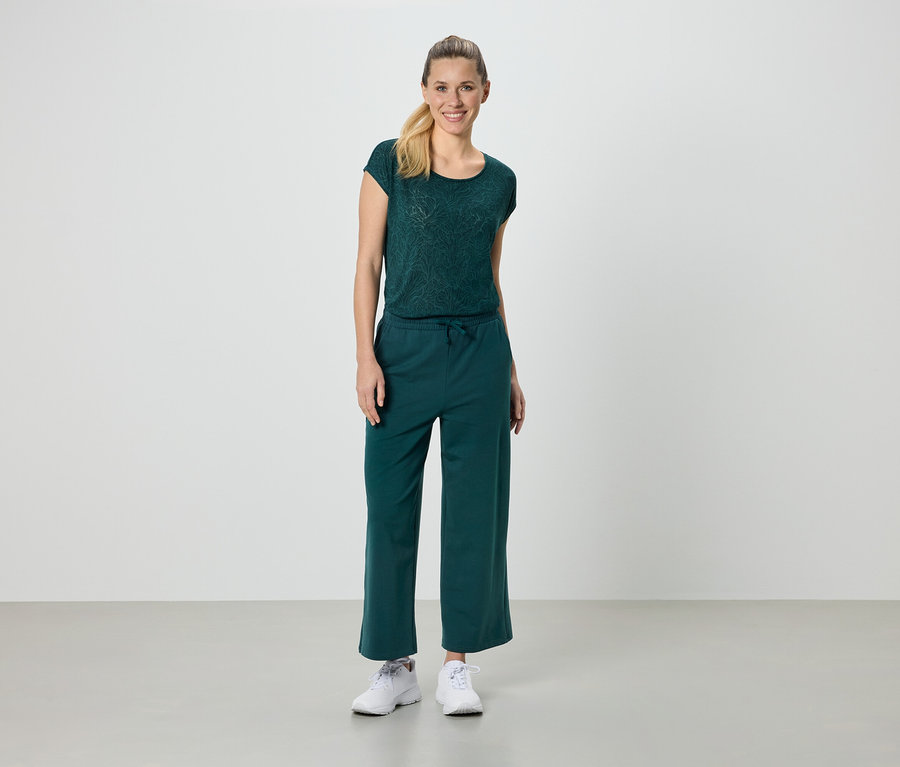 Frau trägt ein grünes T-Shirt und eine grüne Hose und weiße Turnschuhe.