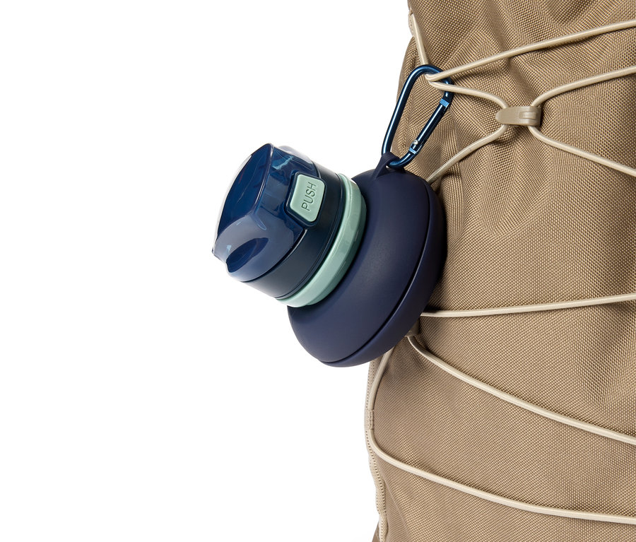 Eine blaue Trinkflasche hängt mit einem Karabiner an einem beigen Rucksack.