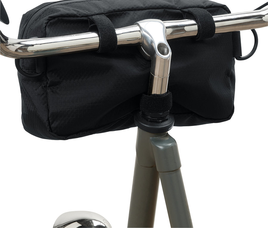 Eine schwarze Fahrradlenkertasche ist mit Klettverschlüssen an einem silbernen Fahrradlenker befestigt.