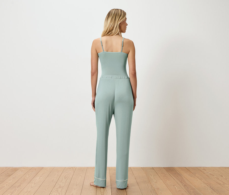 Rückansicht einer Frau mit blonden Haaren, die einen hellgrünen Body und eine passende Hose mit weißem Saum trägt.