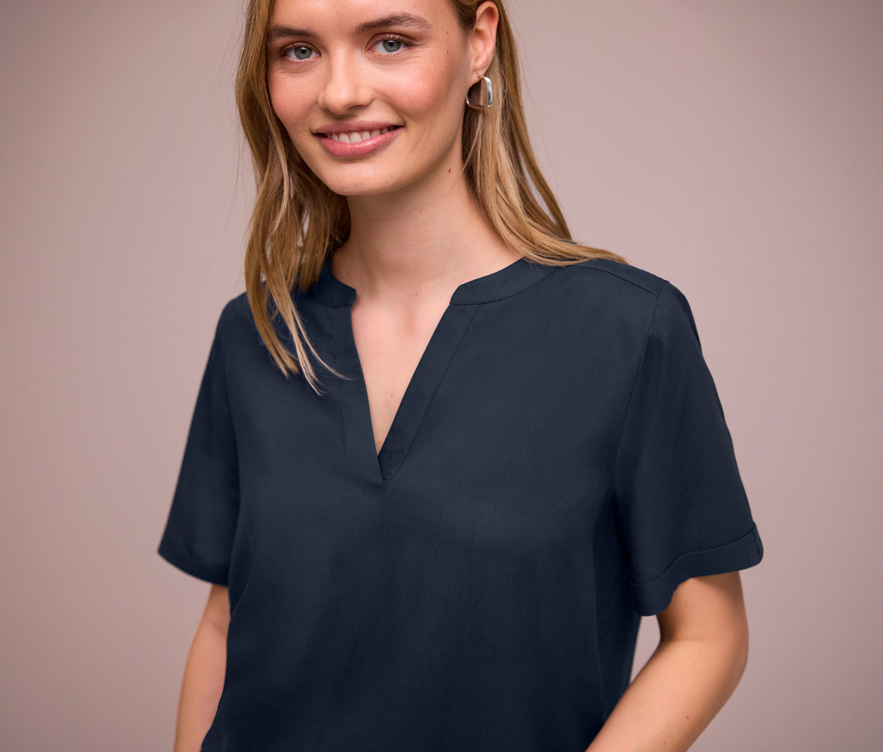 Frau trägt eine dunkelblaue Street One Webbluse mit V-Ausschnitt und silberne Ohrringe.