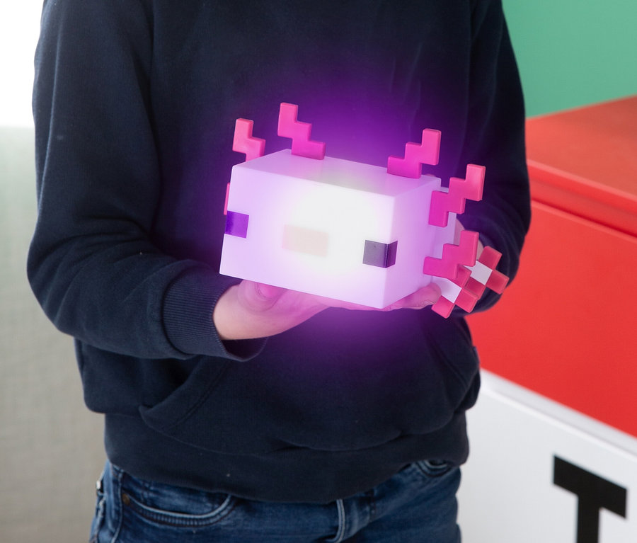Kind hält eine leuchtende, würfelförmige Axolotl-Lampe mit rosa Akzenten.