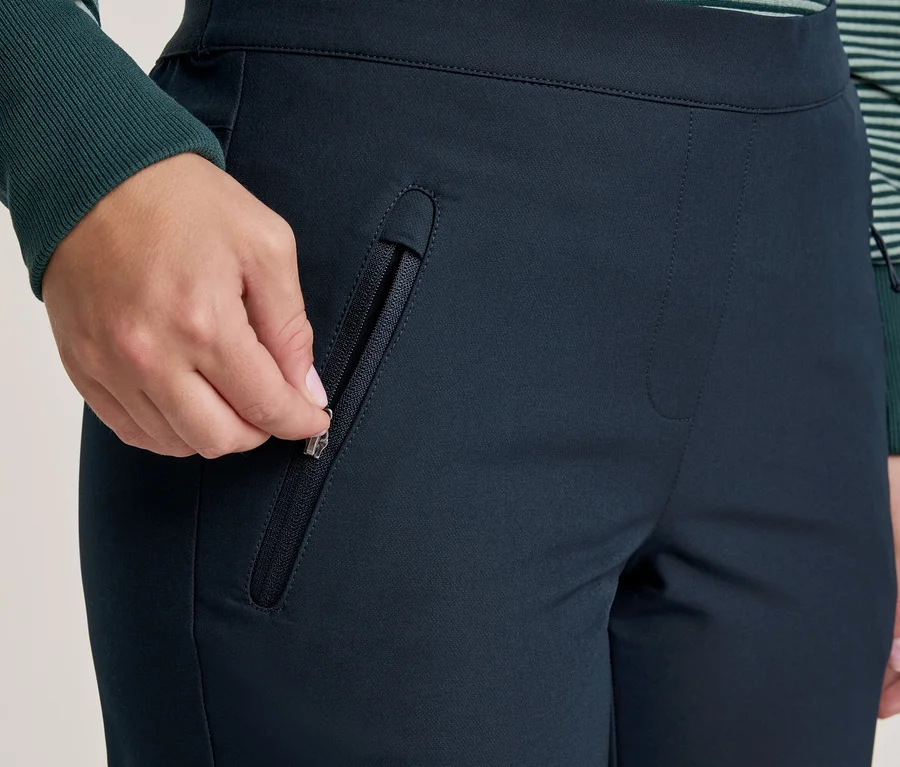Nahaufnahme einer Hand, die eine Tasche an einer dunkelblauen Hose mit Reißverschluss schließt, mit einem grün-weiß gestreiften Ärmel.