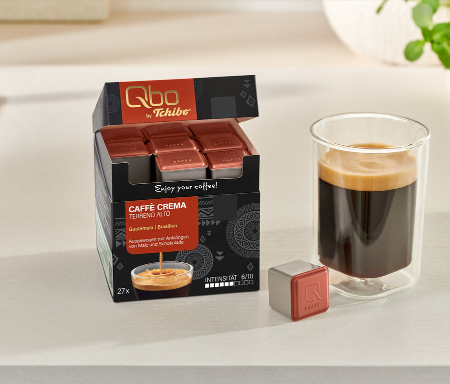 Ein Glas Kaffee steht neben einer geöffneten Packung Qbo Caffè TERRENO ALTO Kapseln und einer einzelnen Kapsel.