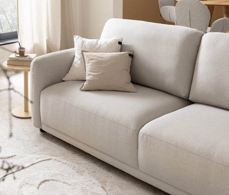 Helles Sofa mit zwei Dekokissen, einem weißen und einem beigen SCHÖNER WOHNEN-Kollektion Dekokissen-Bezug »COAST«, neben einem runden Beistelltisch mit Tasse und Büchern.