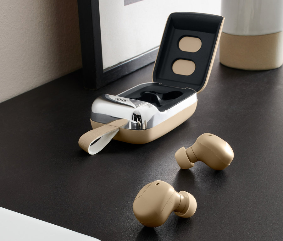 Zwei beige TWS-IN-EAR Kopfhörer und ein offenes Ladecase auf einem Tisch neben einem Handy.