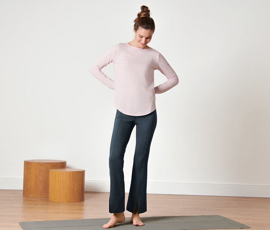 Frau steht auf Yogamatte und trägt eine dunkelblaue Bodyforming-Sporthose.