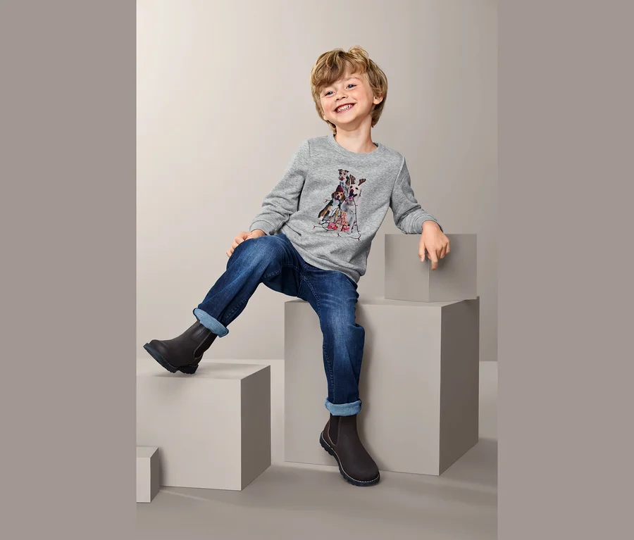 Junge sitzt auf einem Block und trägt ein Sweatshirt und Jeans.