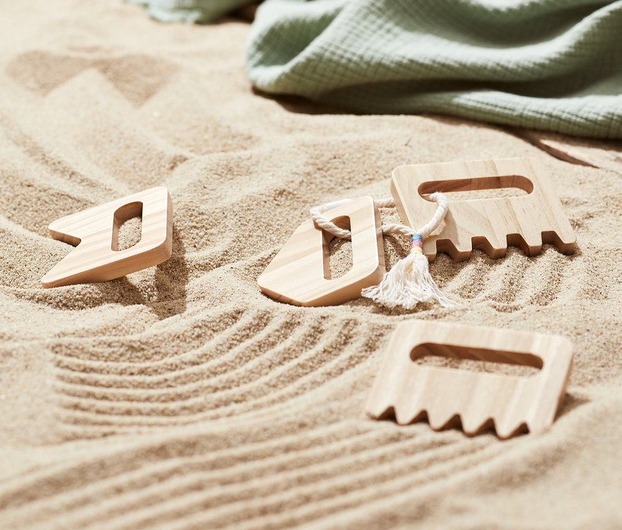 Im Sand liegen drei Kinder-Sandkämme, eine grüne Decke und Flip-Flops.