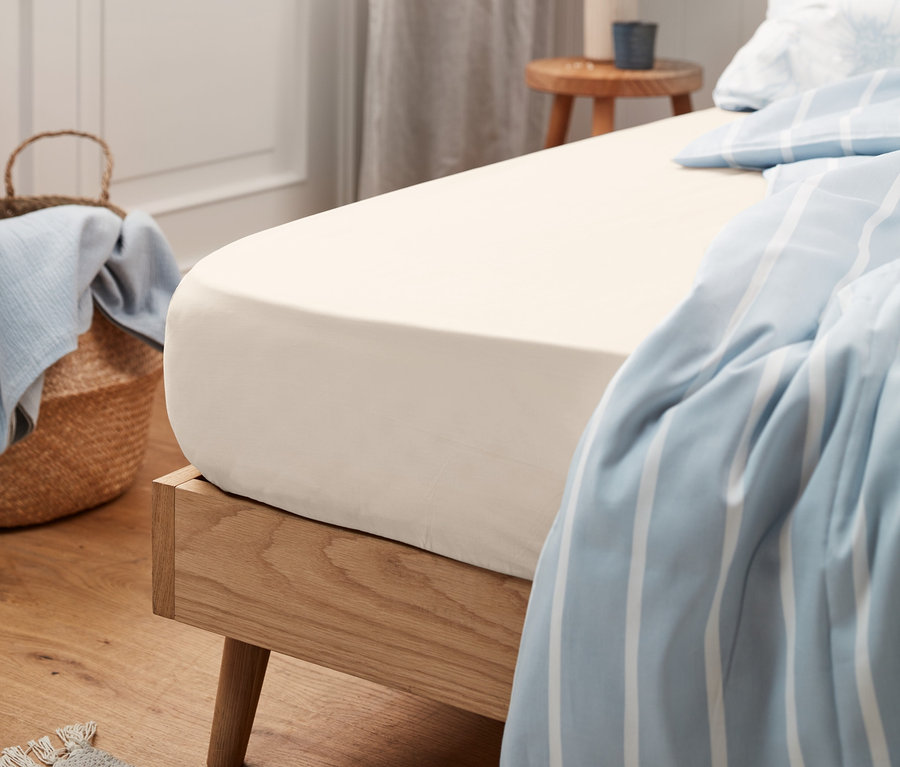 Detailansicht eines beigen Jersey-Spannbettlakens auf einem Bett mit Holzrahmen.