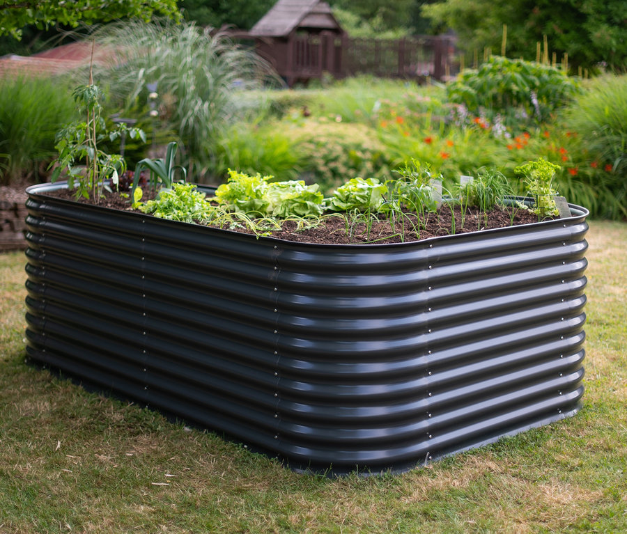 Schwarzes Hochbeet in L-Form mit Pflanzen auf einer Rasenfläche.