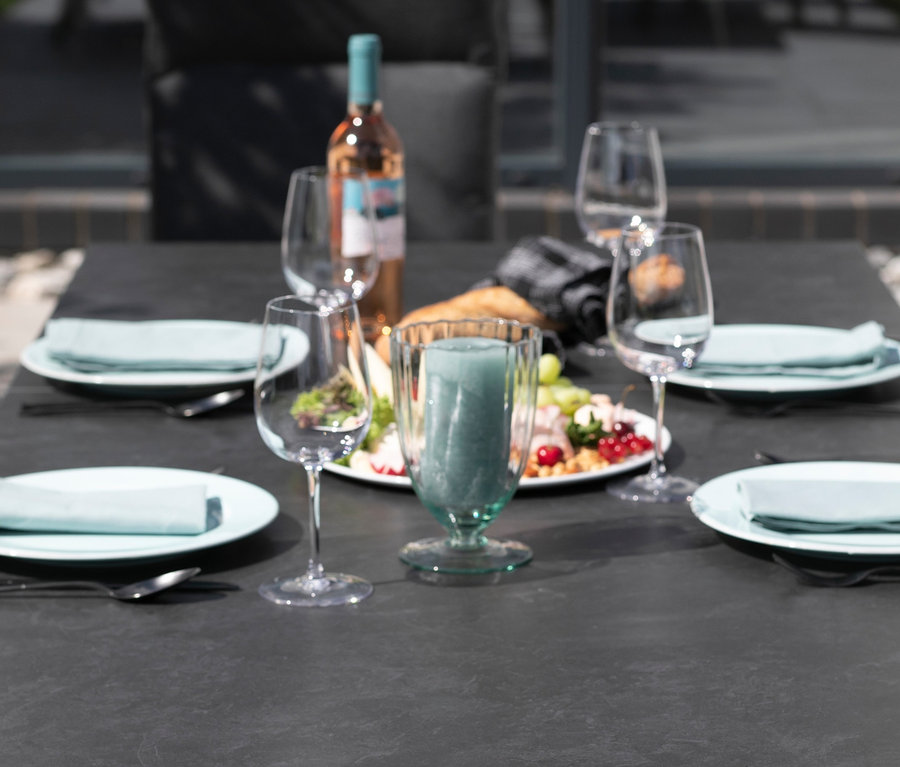 Auf dem Tisch steht ein deVriesAlu Ausziehtisch, 160/210, steingrau, mit Wein, Gläsern, Tellern und Kerze.