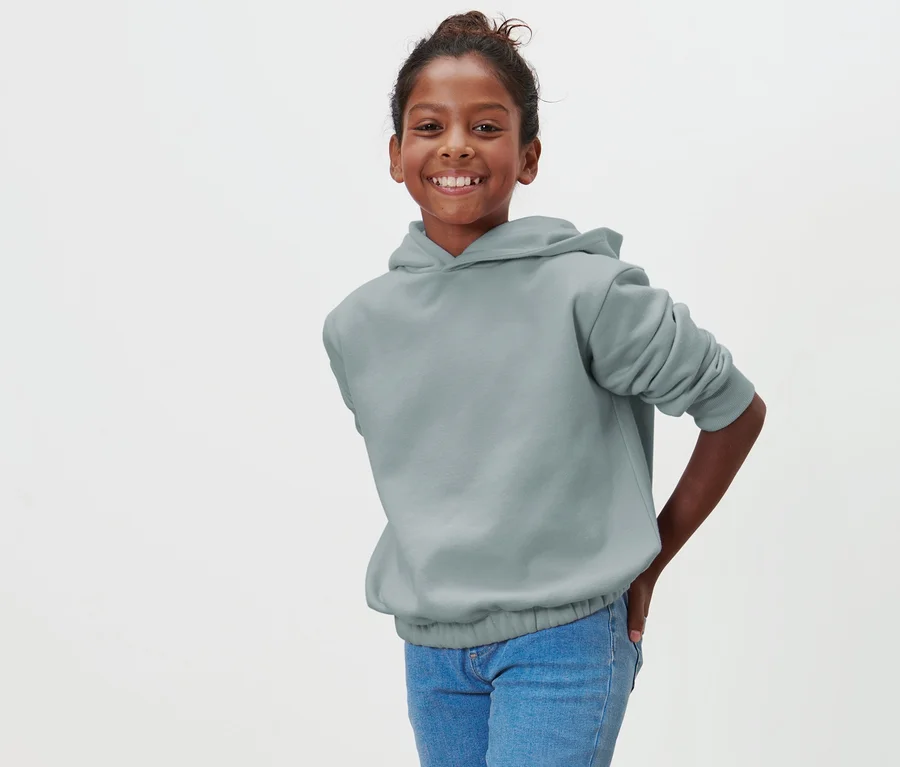 Ein lächelndes Mädchen posiert in einem Kinder-Sweat-Hoodie und blauen Jeans.