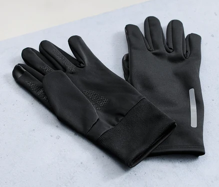 Zwei Paar Windprotection-Thermohandschuhe liegen auf einer grauen Oberfläche, im Hintergrund ein Fahrrad.