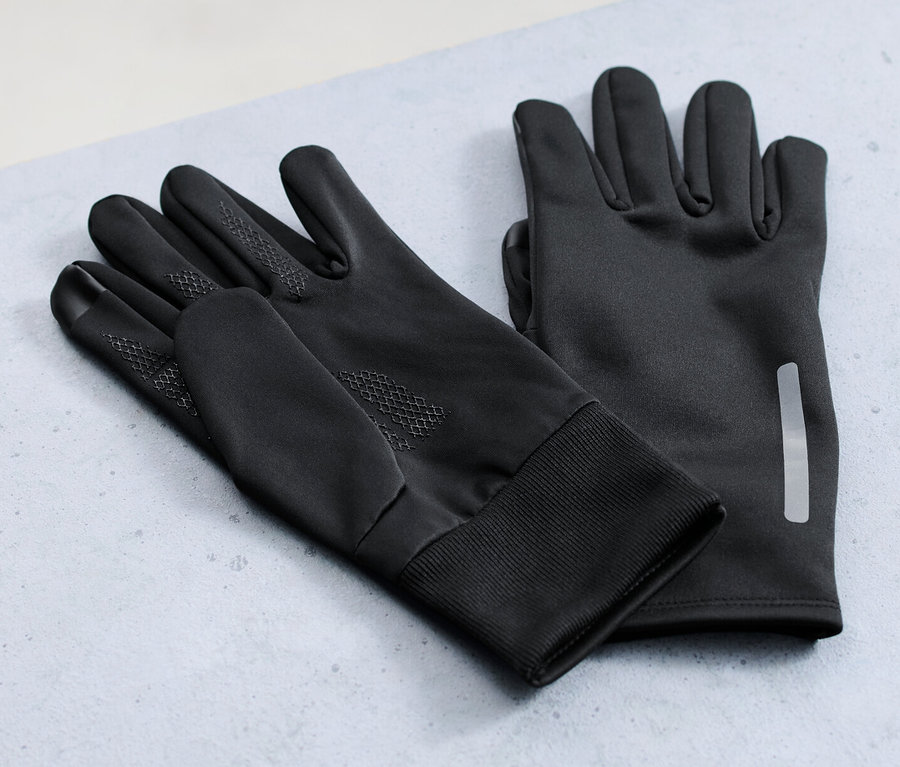 Zwei Paar Windprotection-Thermohandschuhe liegen auf einer grauen Oberfläche, im Hintergrund ein Fahrrad.