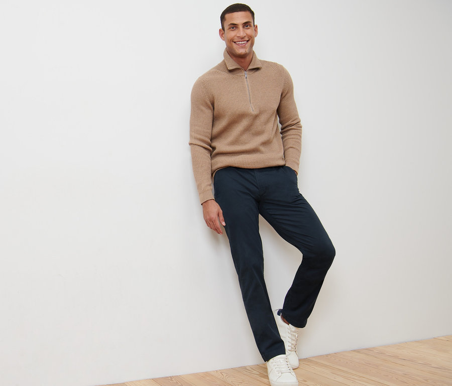 Ein lächelnder Mann lehnt an einer Wand und trägt eine marineblaue Chino.