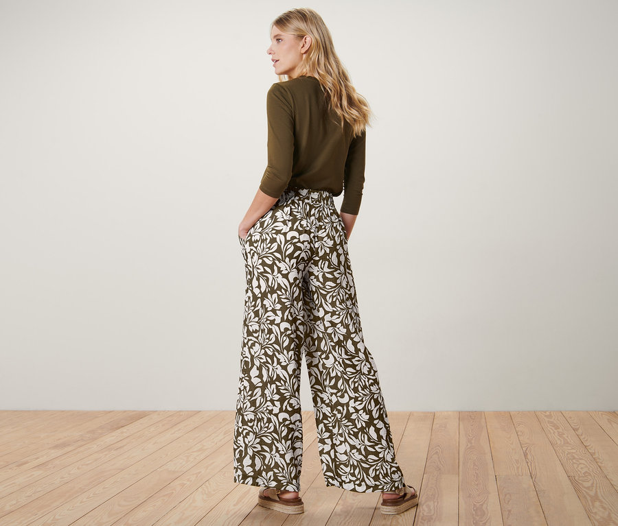 Frau steht mit dem Rücken zur Kamera und hat die Hände in den Taschen der bedruckten Schlupfhose.