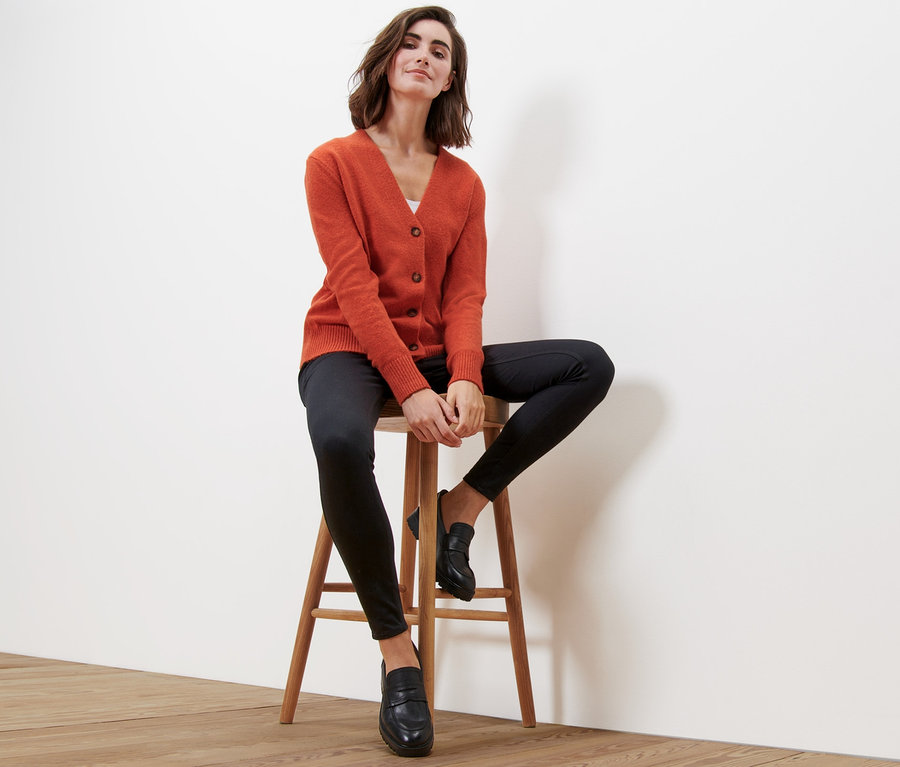 Frau sitzt auf einem Hocker und trägt einen orangefarbenen Cardigan mit V-Ausschnitt.