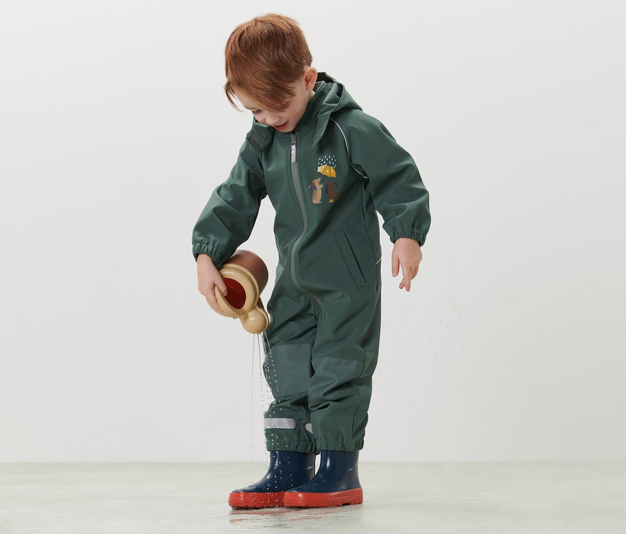 Junge spielt im Kinder-Softshell-Einteiler mit einem Wasserspielzeug.