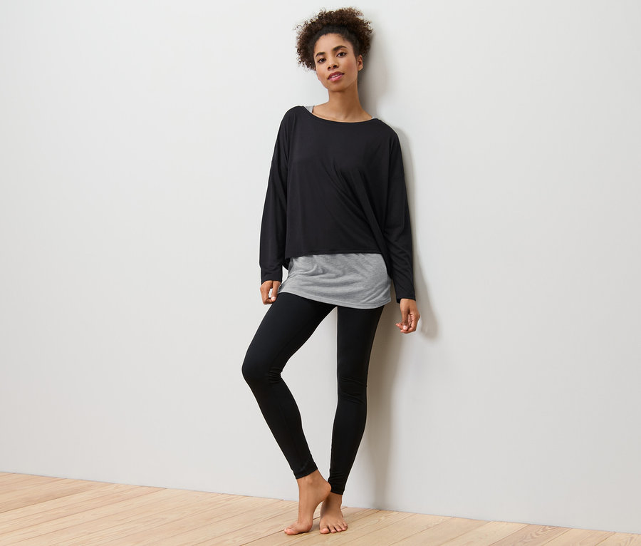 Frau posiert in schwarzem 2-in-1-Sportshirt und schwarzen Leggings.