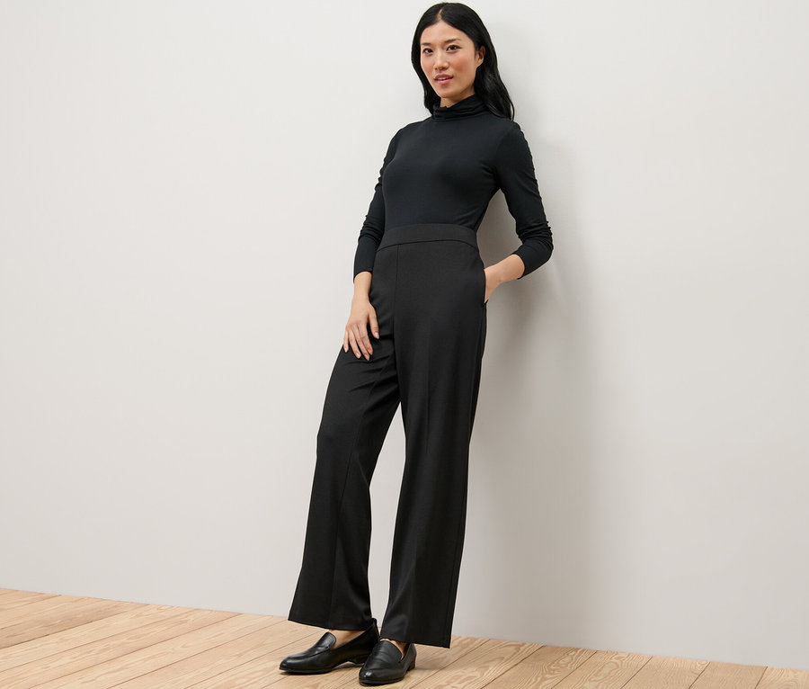 Frau in schwarzem Rollkragenoberteil und Komfort-Jerseyhose lehnt an der Wand.
