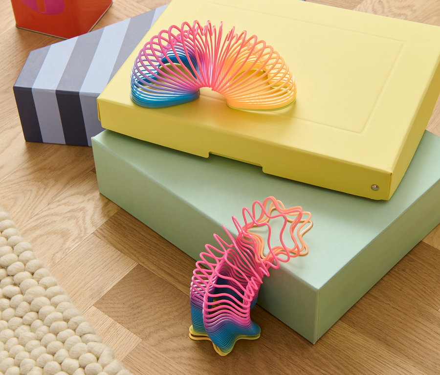 Zwei Treppenhüpfer liegen übereinander auf drei Schachteln und neben einer roten Blechdose auf einem Holzboden.