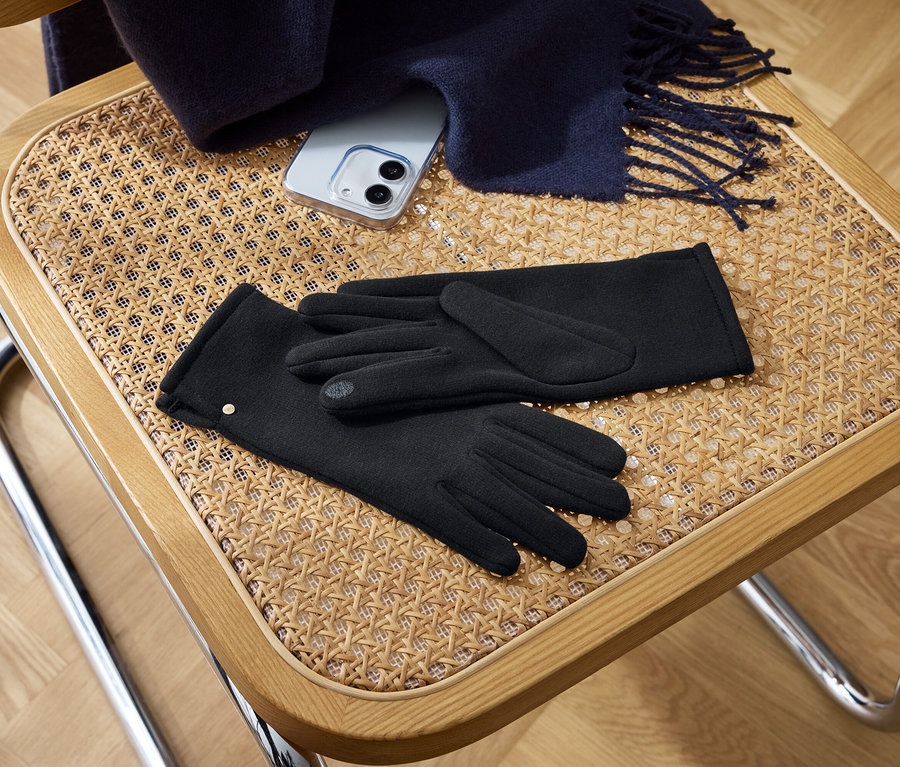 Auf einem Stuhl liegen schwarze Handschuhe, ein Handy und ein Schal.