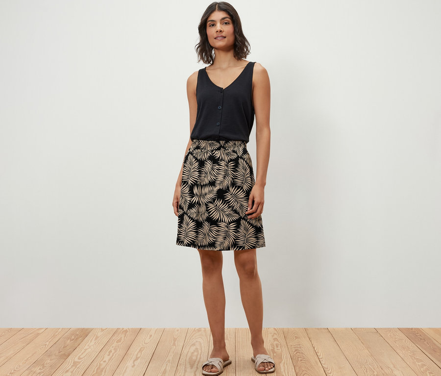 Frau posiert in schwarzem Top und bedrucktem Jerseyrock auf Holzboden.